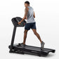 Man running on black Horizon folding treadmill wearing gray sleeveless shirt and navy shorts, shown in profile view on white 