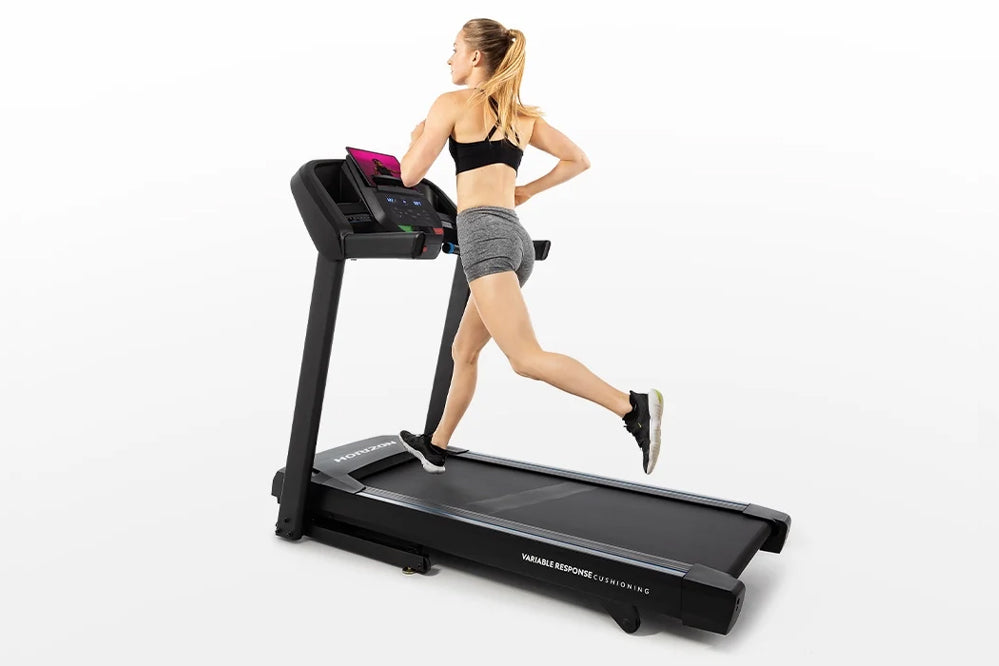 Woman running on black Horizon T101 folding treadmill with digital display, wearing black sports bra and gray shorts