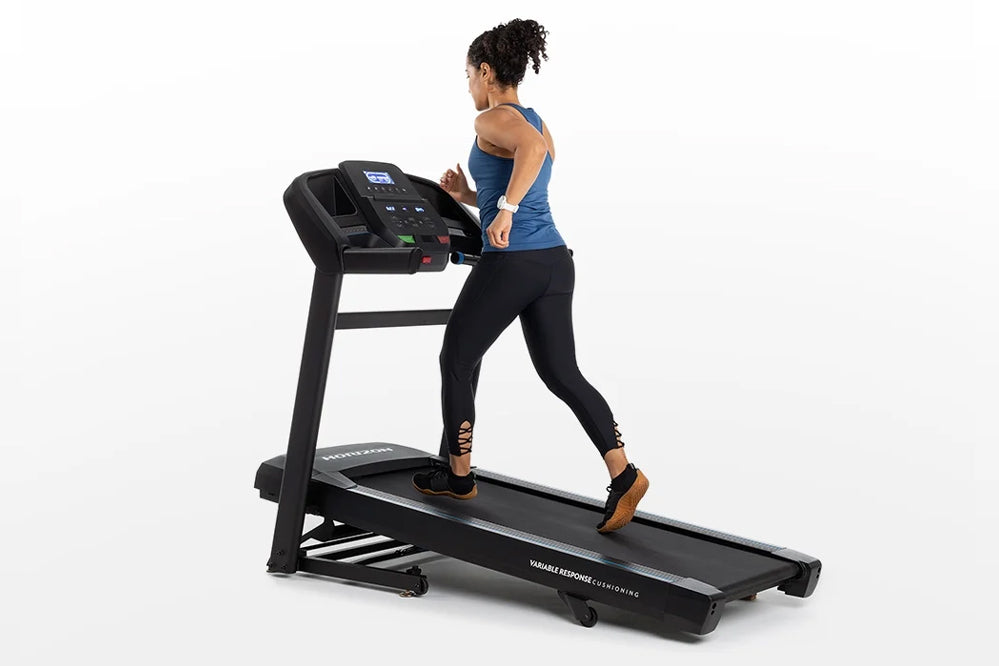Woman running on black Horizon T202 folding treadmill with digital display, wearing blue tank top and black leggings