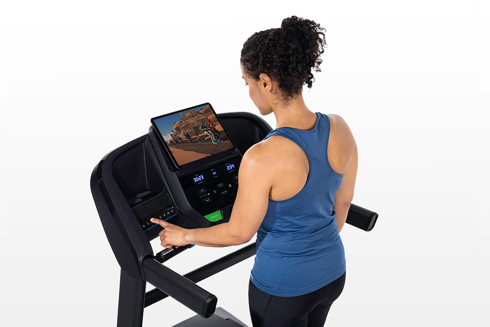 Woman wearing blue racerback tank top and black pants using black Horizon T202 folding treadmill with digital display on whit