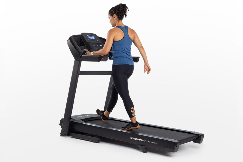 Woman running on black Horizon T202 folding treadmill with digital display, wearing blue tank top and black leggings