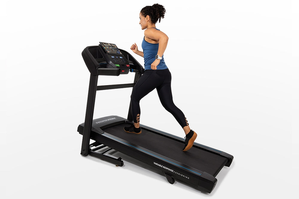 Woman running on black Horizon T202 folding treadmill with blue digital display, worn on white background