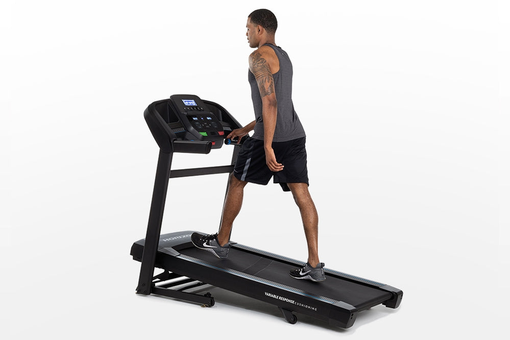 Man using black Horizon folding treadmill with digital display, worn by model on white background