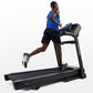 Man running on black Horizon T303 folding treadmill with blue digital display, wearing blue tank top and black shorts on whit