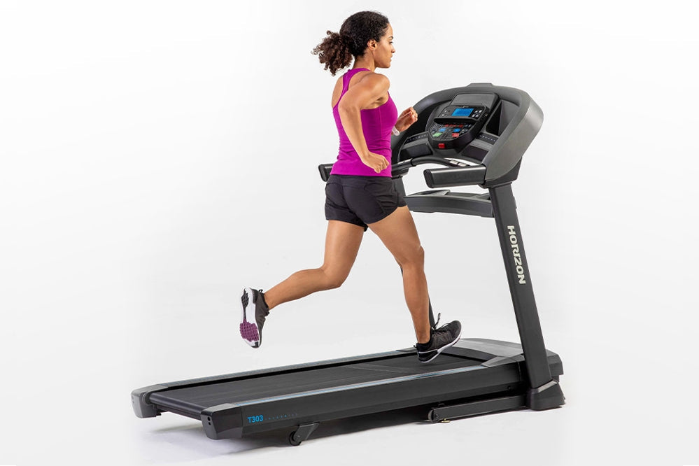 Woman running on black Horizon T303 folding treadmill with digital display, wearing magenta tank top and black shorts