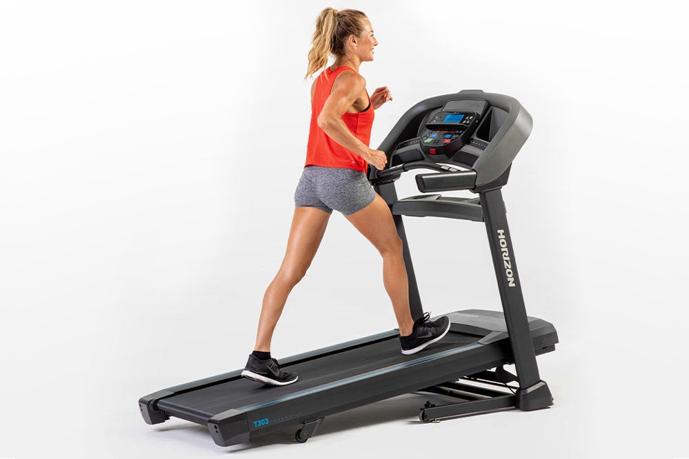 Woman running on black Horizon T303 folding treadmill with digital display, wearing red tank top and gray shorts