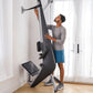 Man using black and silver Hydrow Arc Rower in home gym with large windows, wearing gray shirt and blue shorts