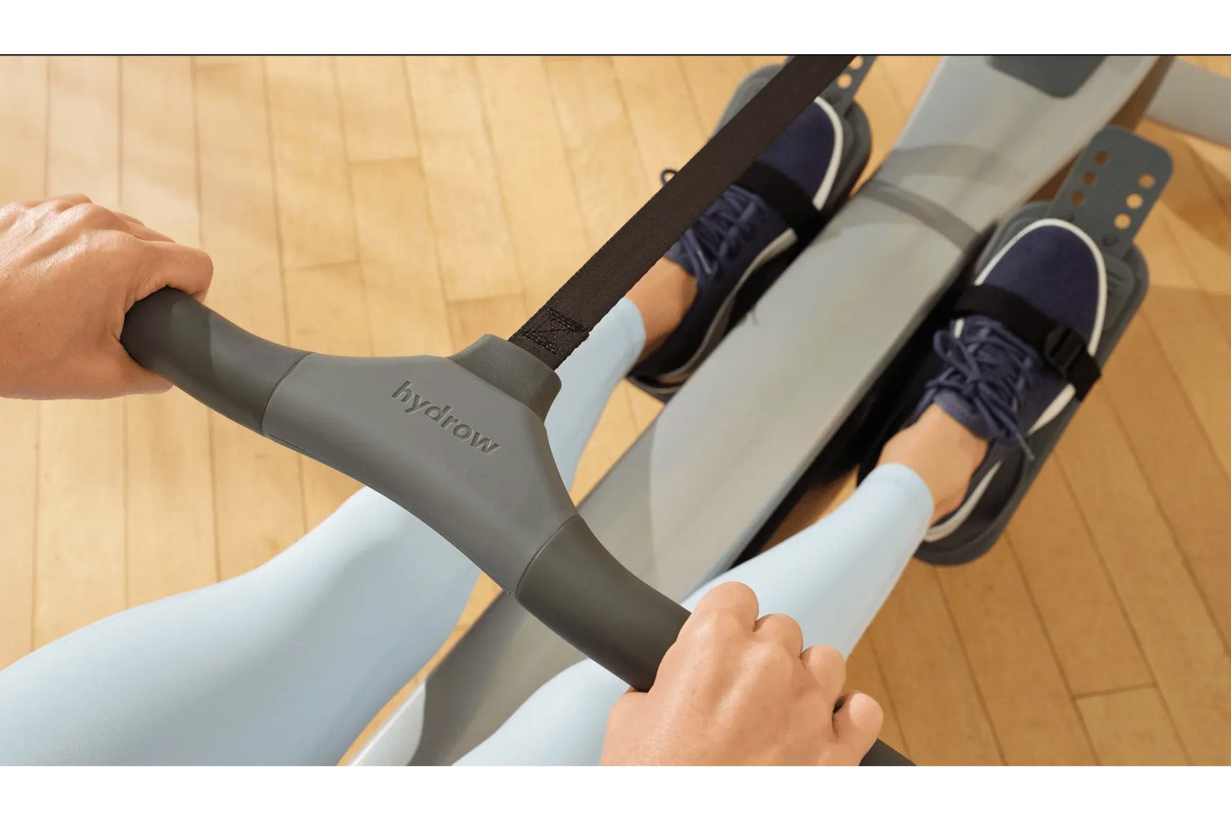 Person using Hydrow Arc rowing machine with gray and black frame, wearing navy shoes and light blue socks