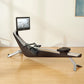 Black and silver rowing machine with attached digital screen displaying water scene, positioned on wooden floor in home inter