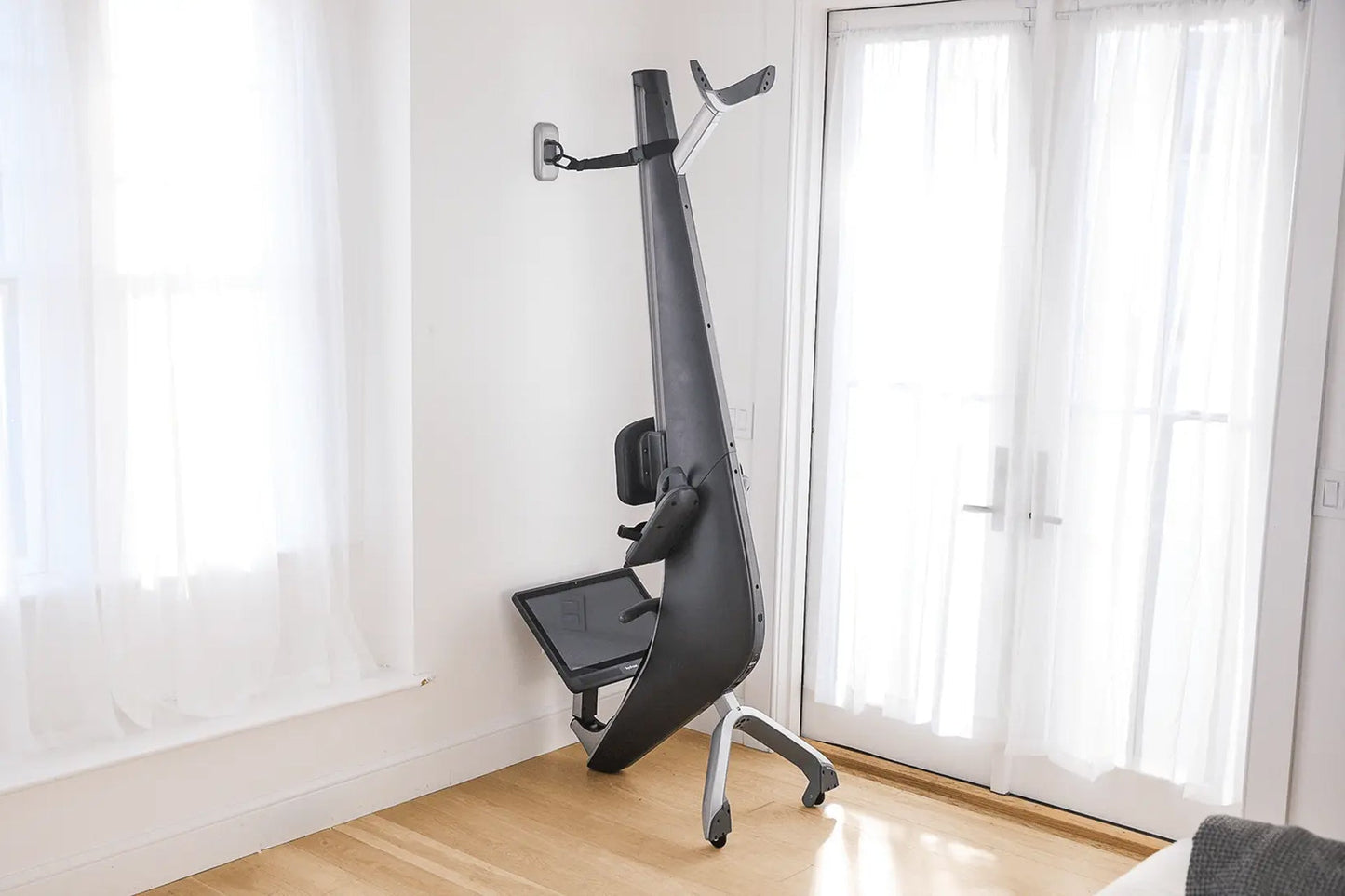 Black and gray Hydrow Origin rowing machine with digital display, footrest, and handle arms, positioned in home interior with