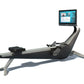 Hydrow Origin rowing machine with black and silver frame, adjustable seat, foot pedals, and mounted touchscreen display showi