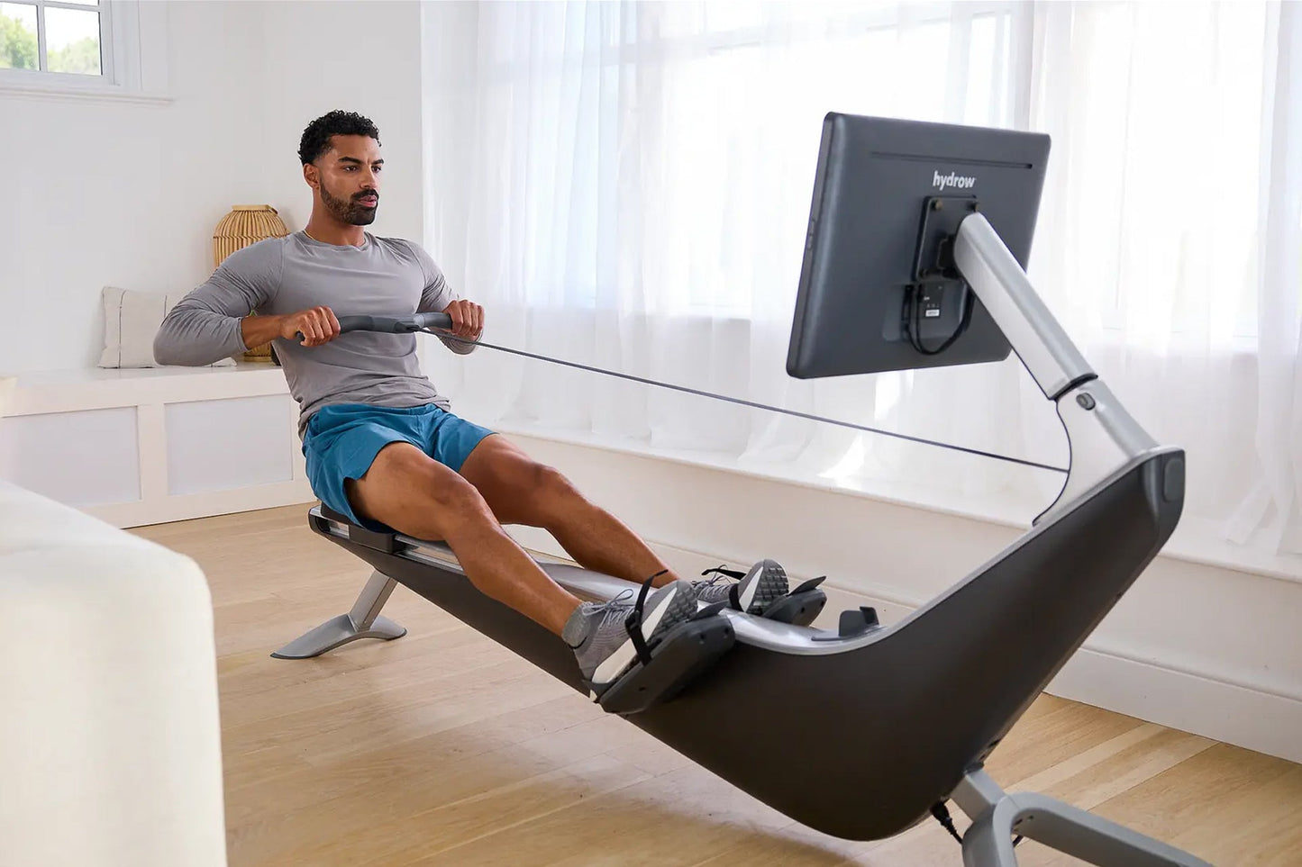 Man using black and silver Hydrow Origin rowing machine with digital monitor in bright home gym setting