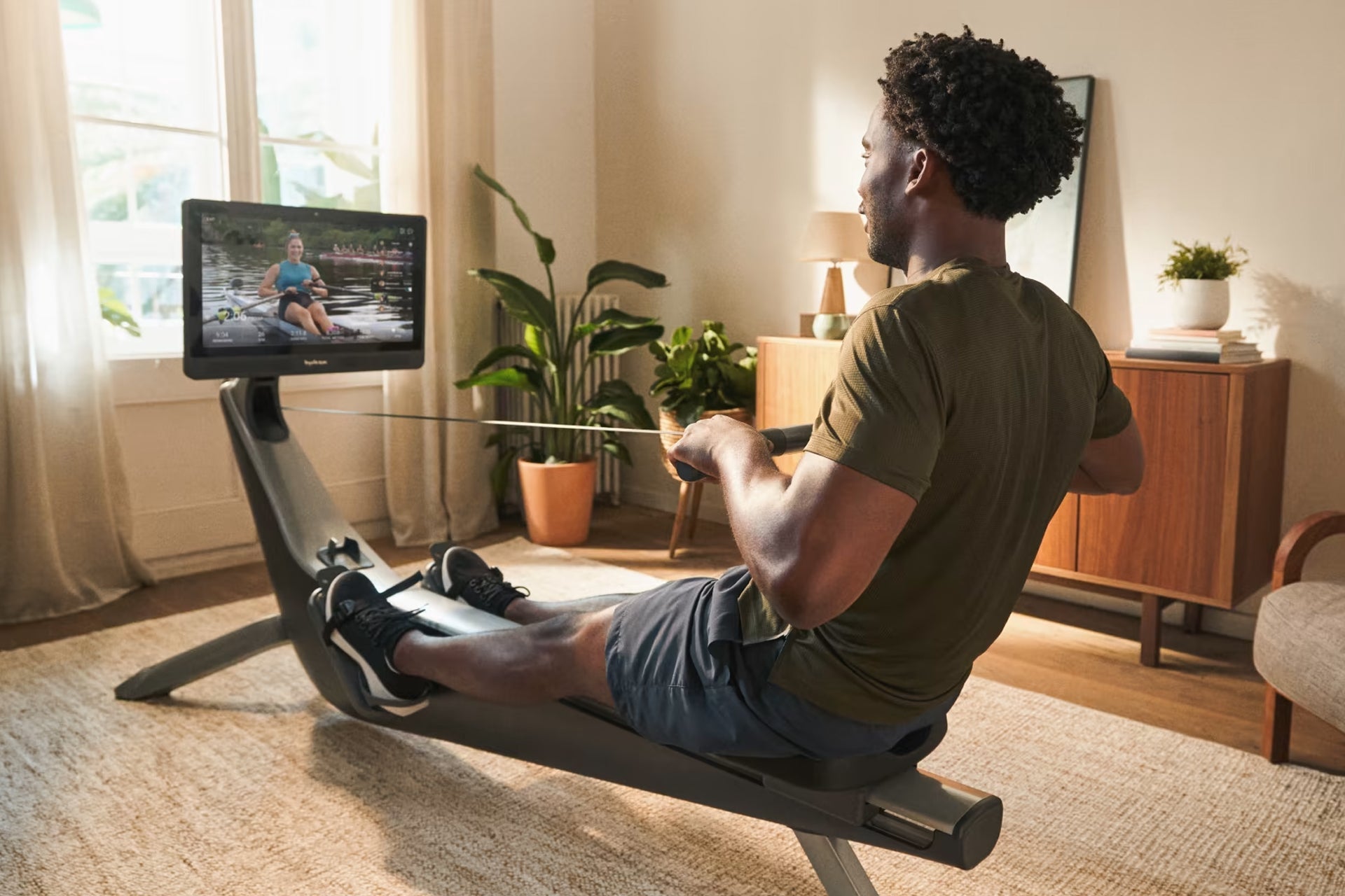 Man using black rowing machine with digital monitor displaying workout content in home gym setting