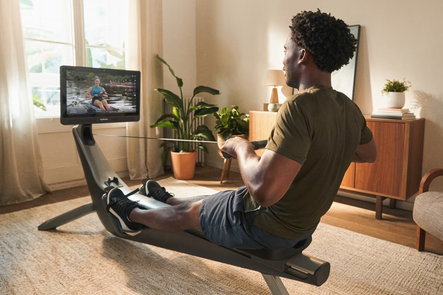 Man using black rowing machine with digital monitor displaying workout content in home gym setting