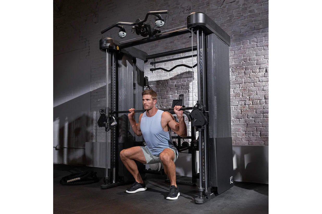 Man using black dual-pulley functional trainer machine with cable attachments in gym setting against brick wall