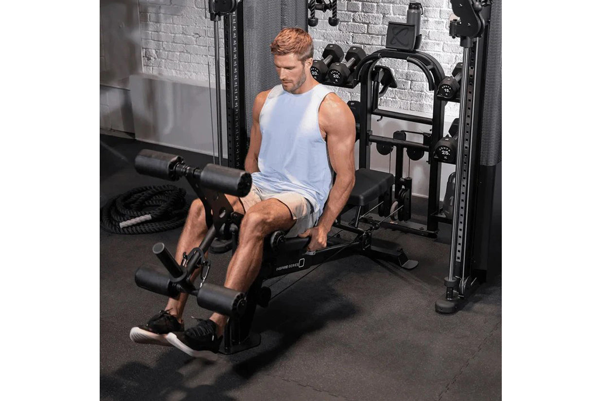 Man wearing light blue sleeveless tank top using black Inspire Fitness FT2 Pro Smith Functional Trainer in gym setting with d