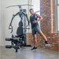 Man using black multi-gym machine with padded seat and cable system in industrial loft space