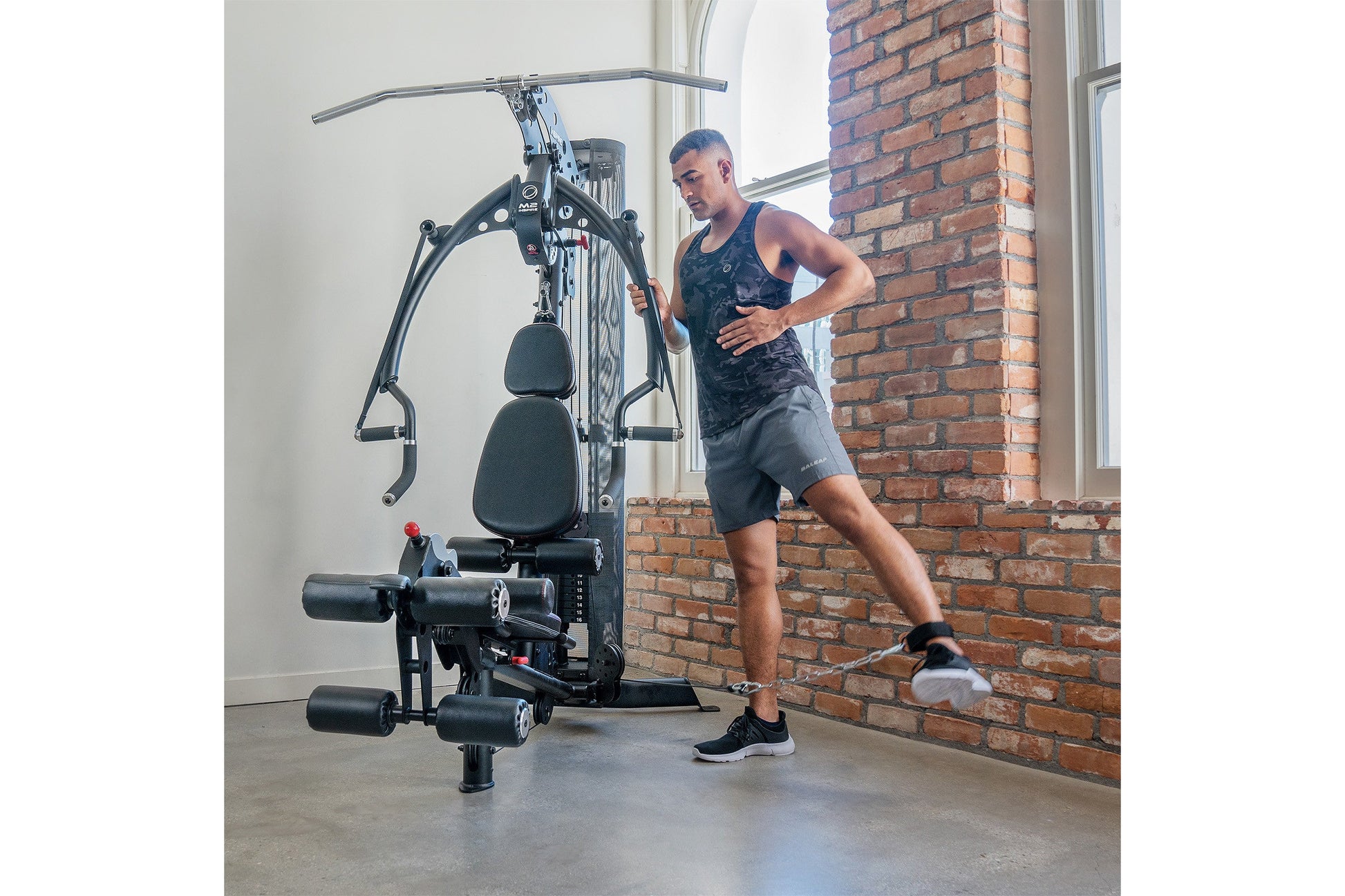 Man using black multi-gym machine with padded seat and cable system in industrial loft space