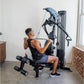Man using blue and black multi-gym machine with leg press and chest press attachments in home gym setting