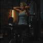 Gray heathered racerback tank top worn by model exercising on black multi-gym equipment in gym setting