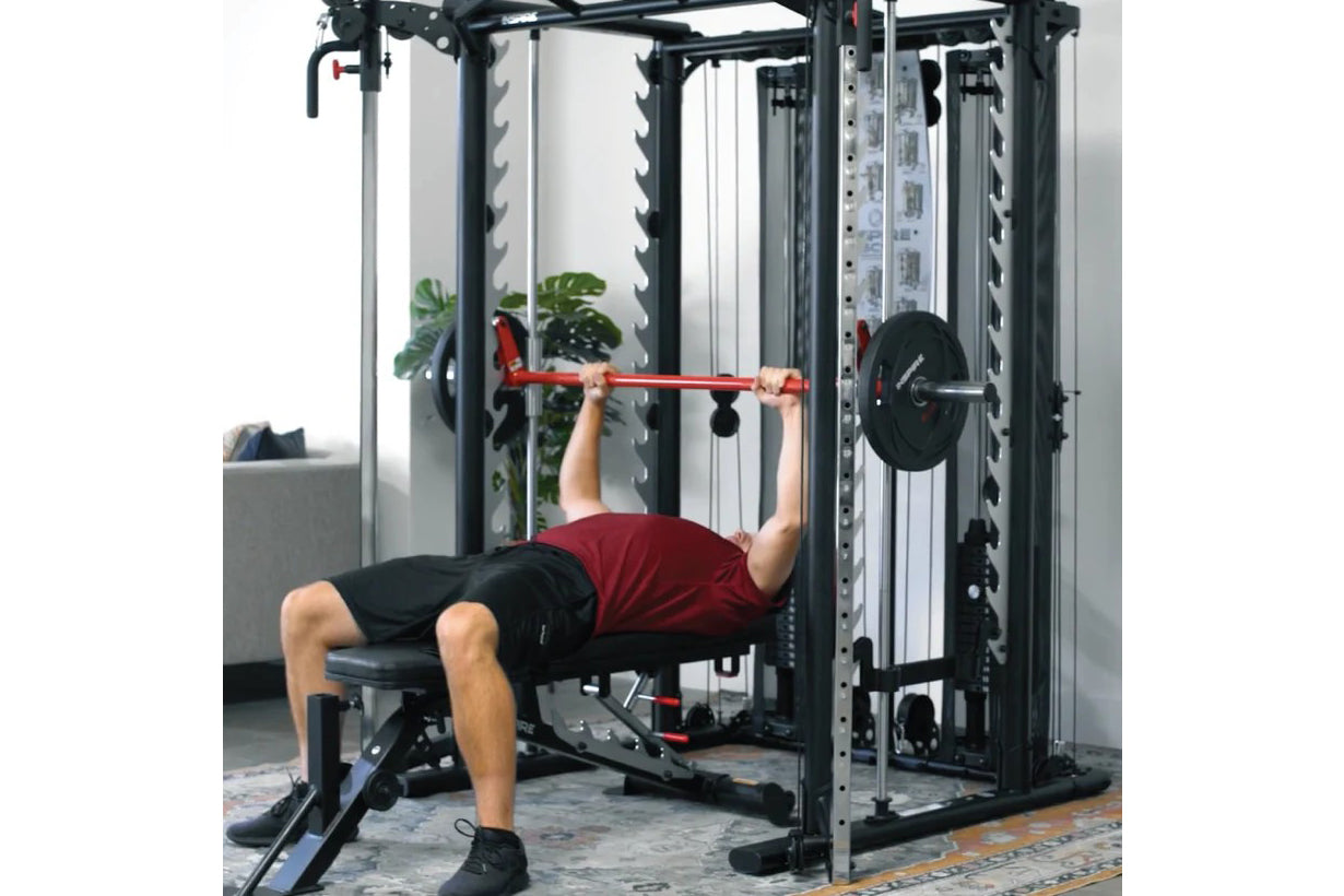 Man performing bench press with red barbell on black and silver Smith cage system in home gym setting