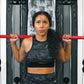 Woman wearing black camo sports bra and leggings holding red barbell across shoulders in gym setting