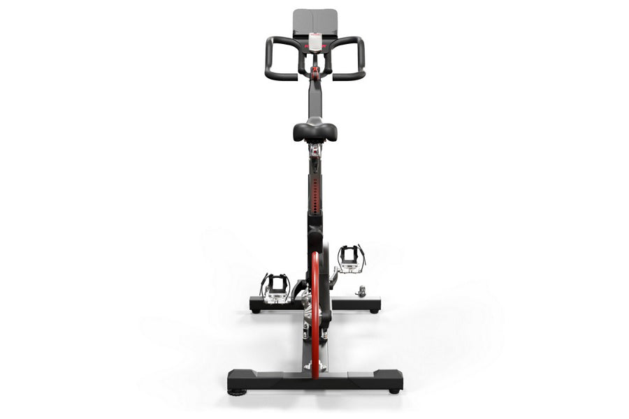 Keiser M3 Indoor Cycle with black and red frame, dual pedals with cages, gray seat and handlebar, digital console on white ba