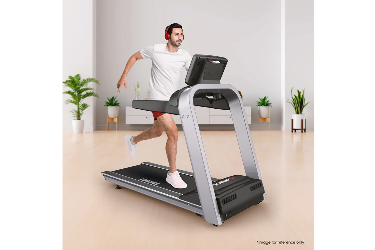 Man running on silver and black Landice L7 treadmill with digital display, wearing white t-shirt and red headphones in home g