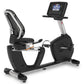 Black and silver recumbent exercise bike with digital console, mesh backrest, and foot pedals on white background