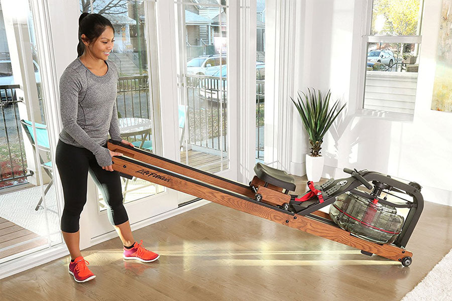 Woman using wooden water rower with red accents in bright home gym space with glass doors