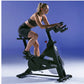 Woman in black sports bra and shorts riding Life Fitness IC3 indoor stationary bike against blue background