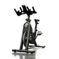 Black and gray stationary indoor exercise bike with padded seat, handlebars, and pedals on white background