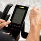 Digital display on a exercise bike with a person's hand interacting with it.