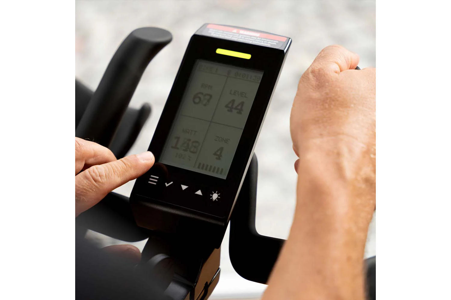 Digital display on a exercise bike with a person's hand interacting with it.
