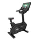 Black upright exercise bike with digital touchscreen display showing fitness class, padded seat with red accents, and stable 