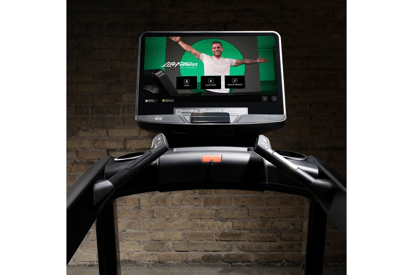 Life Fitness Integrity+ treadmill with black frame and touchscreen display showing fitness app interface against brick wall