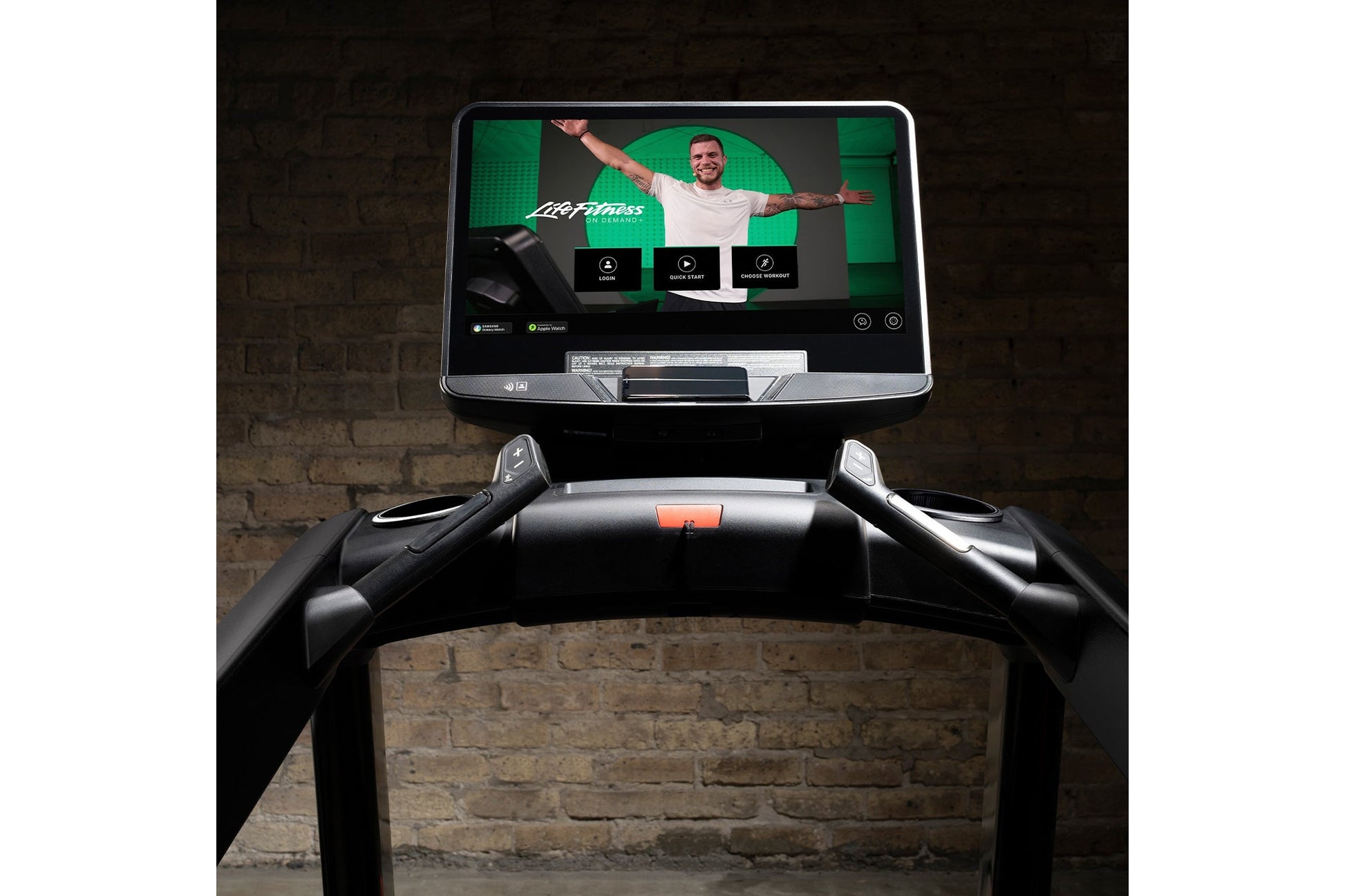 Life Fitness Integrity+ treadmill with black frame and touchscreen display showing fitness app interface against brick wall