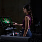 Woman wearing purple sleeveless sports top and navy leggings using Life Fitness Integrity+ treadmill with touchscreen display