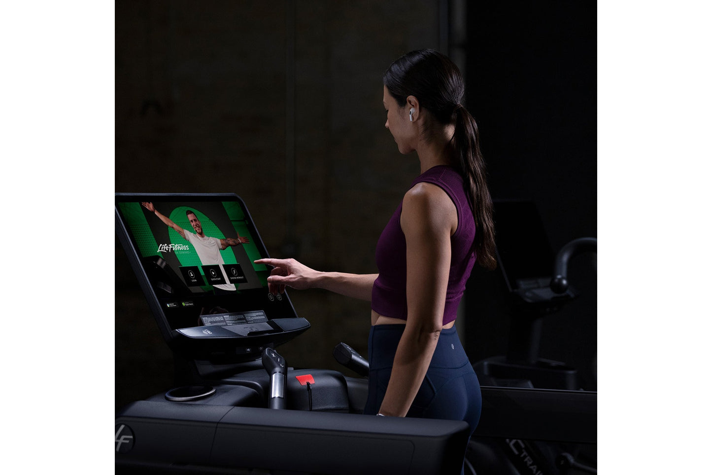 Woman wearing purple sleeveless sports top and navy leggings using Life Fitness Integrity+ treadmill with touchscreen display