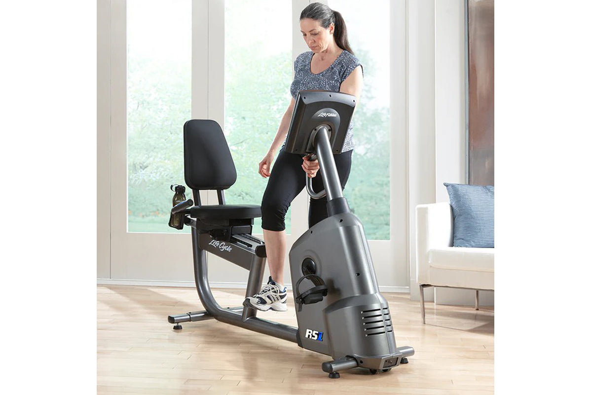 Woman using gray and black Life Fitness RS1 recumbent exercise bike with digital display in bright home gym setting