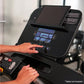 Black Life Fitness Run CX treadmill console with blue digital display showing metrics, operated by user hands in gym setting