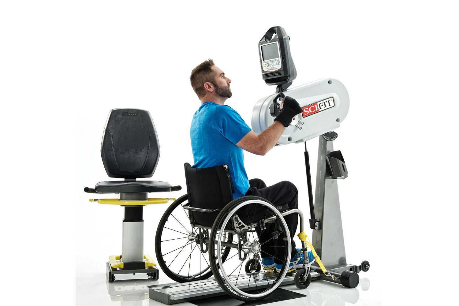 Man in wheelchair using white SCIFIT PRO1 upper body exercise machine with digital display, wearing blue shirt on white backg