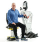 Man in blue jacket seated on white and yellow exercise machine with digital display monitor, white background