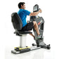 Man in blue shirt exercising on black and gray stationary bike with digital console display, white background
