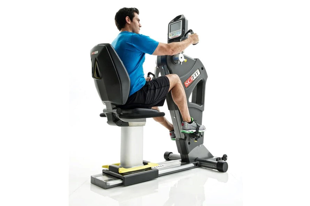 Man in blue shirt exercising on black and gray stationary bike with digital console display, white background