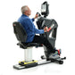 Older man in blue shirt seated on black and white recumbent exercise bike with digital display console, on white background