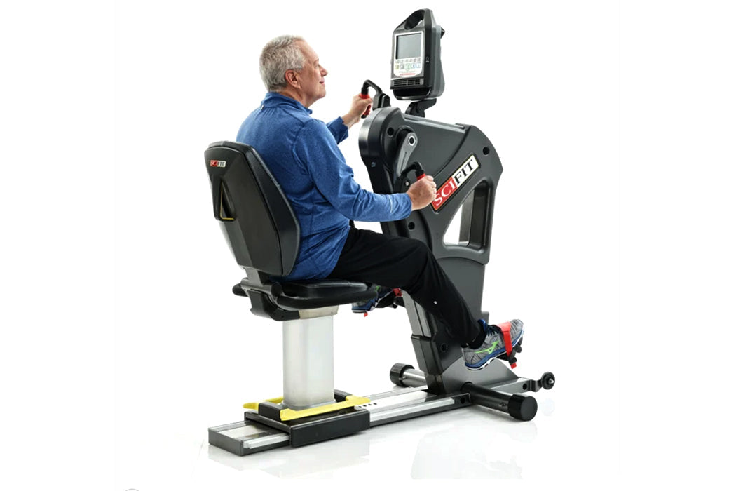 Older man in blue shirt seated on black and white recumbent exercise bike with digital display console, on white background