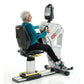 Senior woman using white and black SCIFIT PRO2 stationary exercise bike with digital display monitor, seated on padded black 