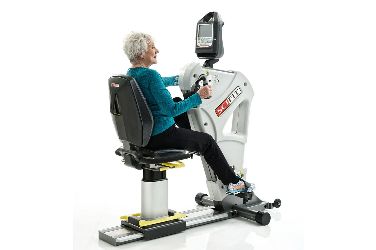 Senior woman using white and black SCIFIT PRO2 stationary exercise bike with digital display monitor, seated on padded black 