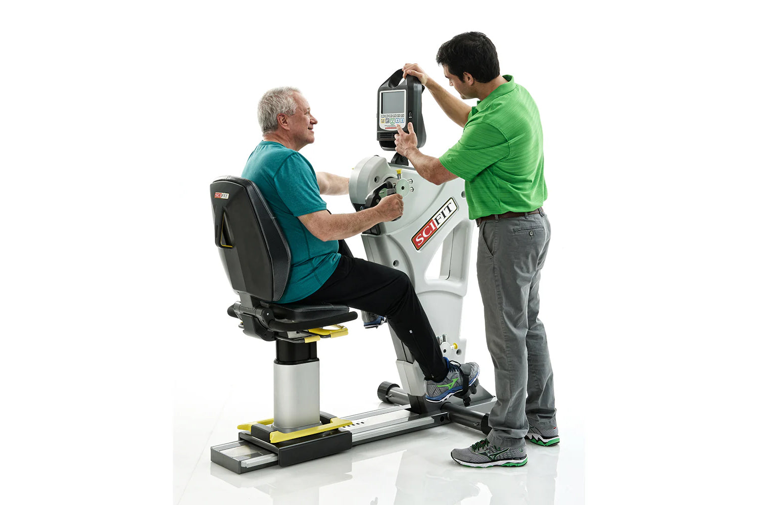 Older man in teal shirt seated on white and black exercise machine with trainer in green shirt adjusting digital monitor abov